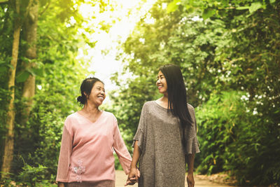 Smiling mother and daughter holding hands against trees