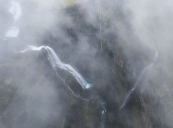 Rapid cascade falling from rough cliff with uneven surface covered with thick mist in gloomy weather in nature of iceland