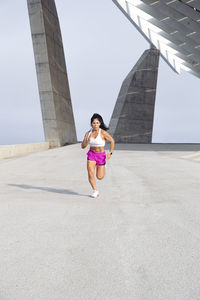 Athlete woman in sportswear running strong through the city. front view