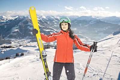 Thoughtful woman holding skis while standing against snowcapped mountains