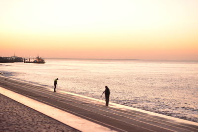 Workers cleaning promenade by sea against clear sky during sunset