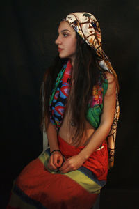 Woman in traditional clothing looking away while sitting against black background