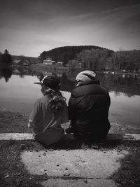 Rear view of people sitting by lake against sky