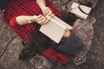 Young woman lying on rock reading book