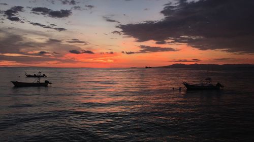 Boats sailing in sea at sunset