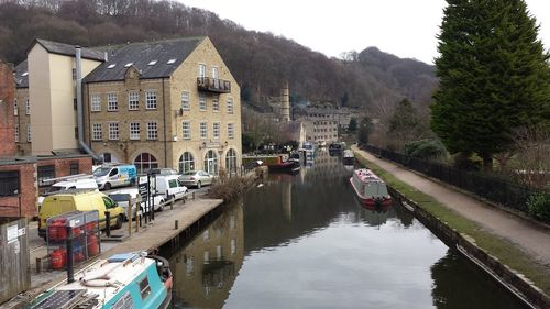 Ferries moored in canal by houses against sky