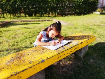 High angle view of girl doing homework on table while sitting in park