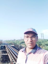 Portrait of young man against railroad tracks against clear sky