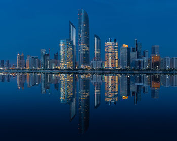 Reflection of illuminated buildings in lake against blue sky