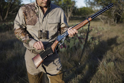 Midsection of man loading bullet in rifle on grassy field