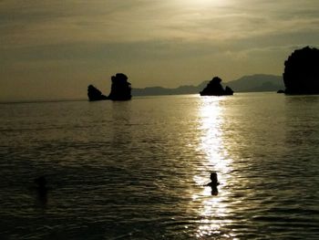 Silhouette people in sea against sky during sunset