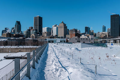 Snow covered buildings in city against clear sky