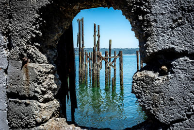 Wooden posts on rocks by sea against sky