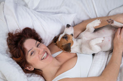 Happy woman with dog relaxing on bed at home