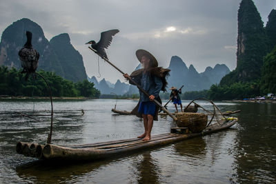Men with birds on wooden rafts in lake against mountains