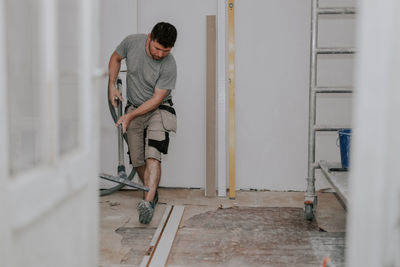 A young man vacuums the floor with a construction vacuum cleaner.