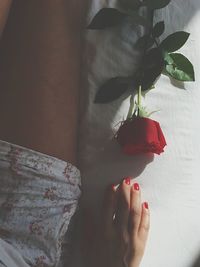 Midsection of woman with rose on bed