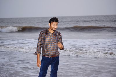 Portrait of young man gesturing peace sign while standing against sea