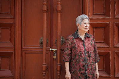 Senior woman standing against door