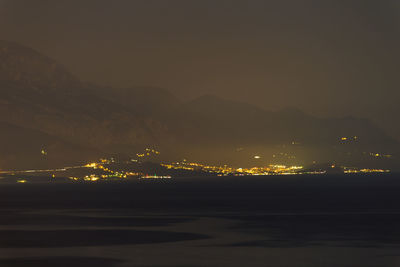 Illuminated mountain by sea against sky at night