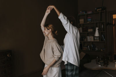 Carefree non-binary couple dancing with each other at home