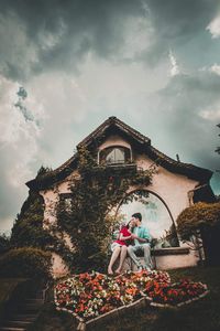 Low angle view of woman sitting by building against sky