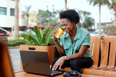 A beautiful african woman drinks coffee in a cafe and works at a laptop, headphones and a phone 