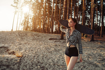Woman with skateboard walking in forest