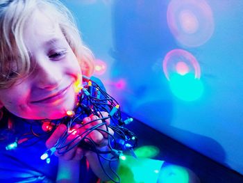 Close-up of boy playing with illuminated string lights at home
