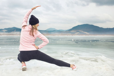 Full length of woman exercising at beach against sky