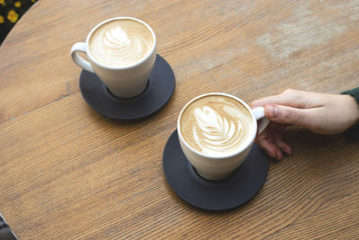 High angle view of coffee cups on table with female hand