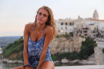 Portrait of woman sitting against sky in city