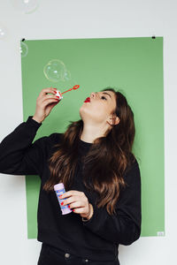 Young woman blowing bubbles against blackboard on wall