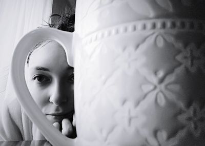 Portrait of young woman seen through coffee cup handle on table