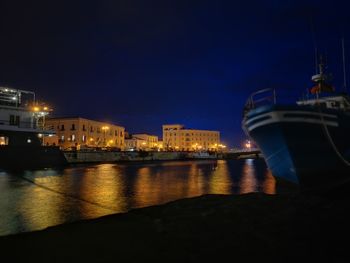 Illuminated city by sea against sky at night