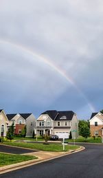 Rainbow over houses by buildings against sky