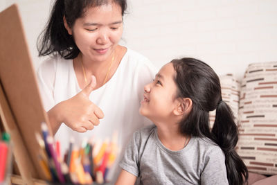 Mother showing thumbs to daughter at home