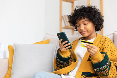 Young woman using mobile phone while sitting on sofa at home