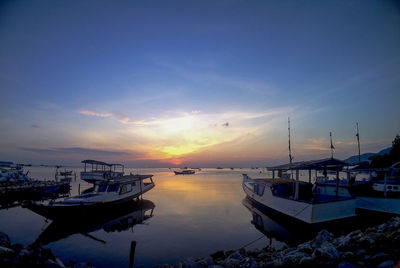 Boats moored in harbor at sunset