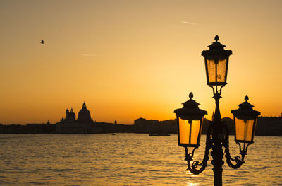 Silhouette street light with canal in background against clear orange sky