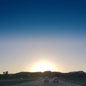 Cars on landscape against clear sky during sunset