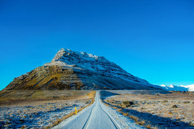 Road by snowcapped mountain against blue sky
