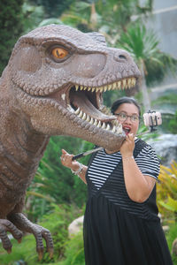 Woman taking selfie with dinosaur statue in park