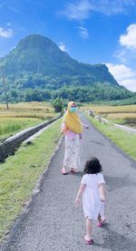 Rear view of mother wearing mask with daughter on road against sky