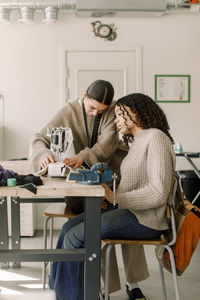 Teacher assisting female student looking at sewing machine in art class at high school