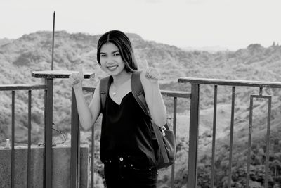 Portrait of young woman standing against railing