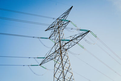 Low angle view of electricity pylon against clear blue sky