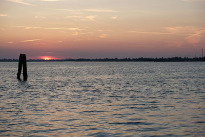Silhouette person standing in sea against sky during sunset