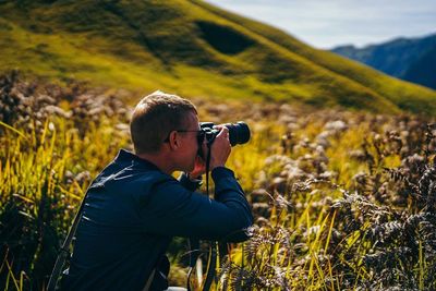 Side view of man photographing with camera while standing on grassy field