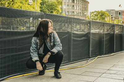 Young woman crouching on footpath in city
